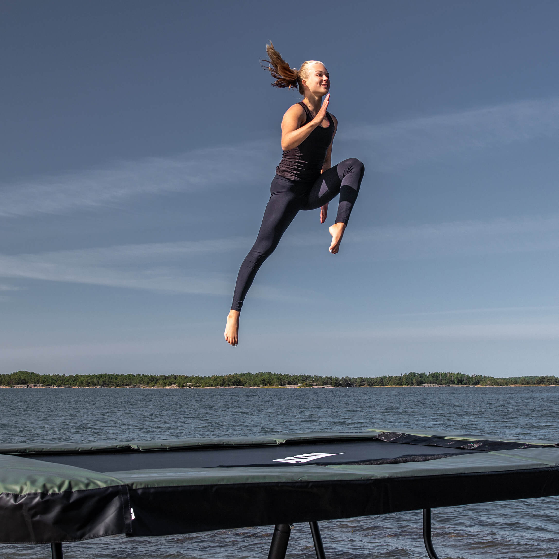 A gymnast jumps on an Acon 13 Sport HD trampoline in an archipelago landscape.
