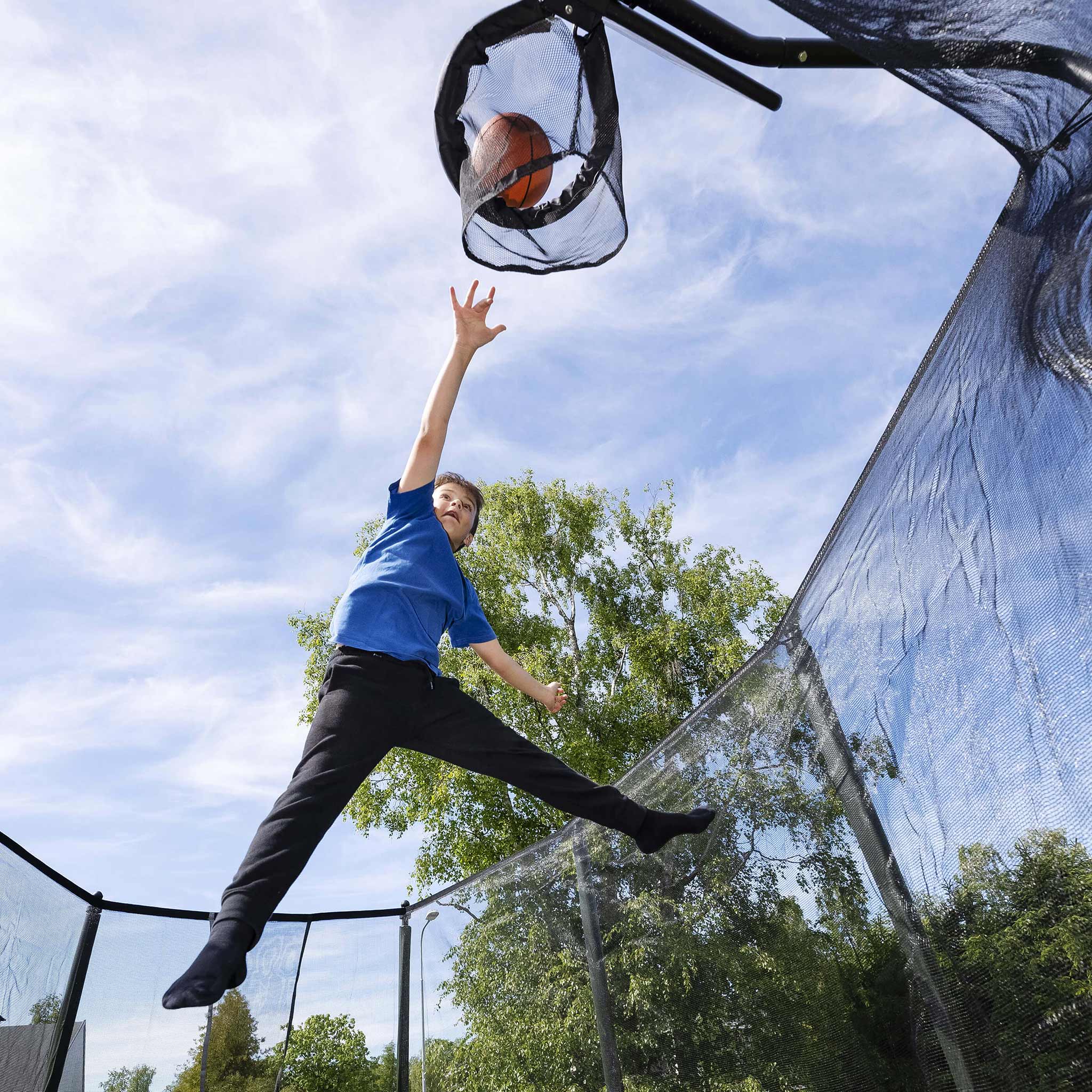 A boy throws a basketball into the trampoline basketball hoop.