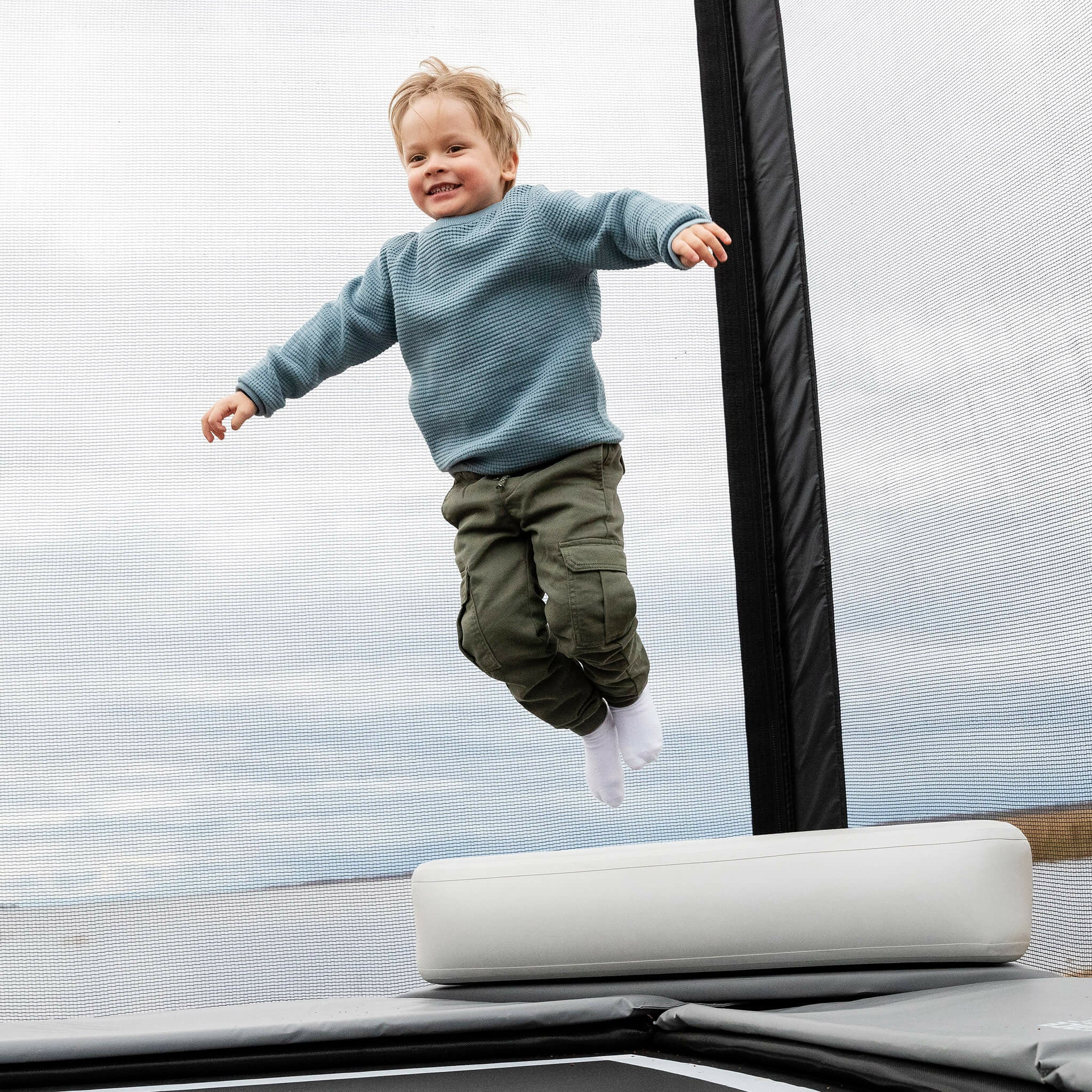 A little boy jumps from the top of the Acon X Inflatable Triangle Block onto a trampoline.